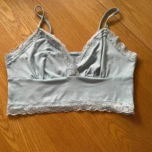 Ljusblå ribbad linnetopp med spetsdetaljer - Säljer en söt ljusblå ribbad linnetopp med smala axelband och spetsdetaljer längs kanterna. Toppen har en v-ringad design och är perfekt för varma dagar.