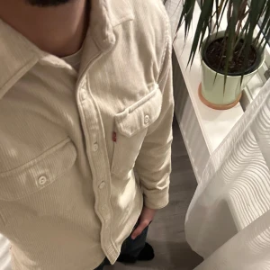 Beige manchester overshirt från Levi's - Säljer en snygg beige manchester overshirt från Levi's. Skjortan har långa ärmar och två bröstfickor med knappar. Perfekt för en stilren look. Passar Storlek S/M (har själv storlek M och passar mig perfekt) För mer bilder / frågor skriv !