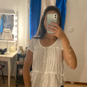 Vit randig blus från H&M med knyt - Säljer en söt vit blus från H&M i storlek 40. Blusen har tunna vertikala ränder, knappar framtill och knytband i midjan för en snygg passform. Kortärmad och med rund halsringning, perfekt för ljusa dagar. Passar s och xs också då den har justerbara band 