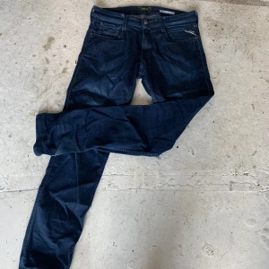 Replay Anbass mörkblå jeans W30 L32 - Snygga mörkblå Replay Anbass jeans med klassisk femficksdesign och raka ben. Jeansen har en slim passform och är tillverkade i mjukt jeansmaterial som sitter skönt. Perfekt för dig som gillar stilrena och tidlösa jeans med cool vibe.