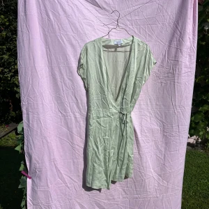 Ljusgrön omlottklänning & Other Stories - Superfin ljusgrön omlottklänning från & Other Stories med knyt i midjan och v-ringning. Kort ärm och luftig känsla, perfekt för varma dagar. Tillverkad i 100% lyocell och 100% viskos i innertyget för en mjuk och sval look.