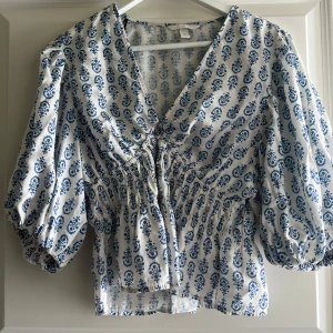 Blommig blus med puffärm från H&M - Säljer en vit blus från H&M med blått blommigt mönster och v-ringning. Storlek L men passar M🌸