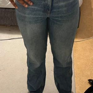 Blå raka jeans med hög midja - Säljer ett par blå jeans med rak passform och hög midja. Jeansen har klassisk femficksdesign och är tillverkade i ett slitstarkt denimtyg. Färgen är en snygg tvättad blå som ger en cool vintagekänsla. Perfekta att matcha med sneakers eller boots.