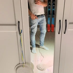 Ljusblå skinny jeans från Nudie - Säljer ett par ljusblå skinny jeans från Nudie med klassisk femficksdesign och snygga detaljer på bakfickorna. Jeansen har låg midja och är tillverkade i mjukt bomullstyg med stretch för skön passform. Perfekta för dig som gillar en smal siluett och stilren look.