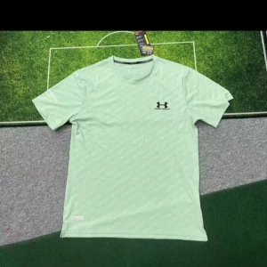 Ljusgrön t-shirt från Under Armour - Fräsch ljusgrön t-shirt från Under Armour med klassisk logga på bröstet. T-shirten har rund hals och korta ärmar, perfekt för träning eller chill. Materialet är lätt och andas, vilket gör den skön att bära när du är aktiv.