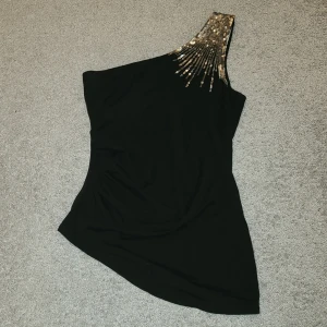 Svart oneshoulder topp från Twentyone - Snygg svart oneshoulder topp från Twentyone med glittrande paljettdetaljer på axeln. Perfekt för en kväll ute eller en festlig tillställning✨️