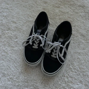 Svarta Vans Old Skool sneakers 36.5 - Svarta Vans Old Skool sneakers med klassisk vit sidorand och vita snören. Skorna har en låg profil, rund tå och platt sula. Materialet är en mix av mocka och canvas, vilket ger en skön och cool vibe. Perfekta för dig som gillar streetstyle och skatekänsla.