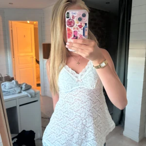 Vit spetsig linnetopp med rosett - Superfin vit linnetopp i spets med v-ringad hals och liten rosett framtill. Toppen är ärmlös och har tunna axelband, perfekt för dig som gillar romantisk och feminin stil. Luftig och lätt, passar till jeans eller kjol för en söt look. vet inte vilket varumärke stod nåt på lappen men känner ej till! 