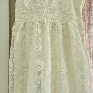 Vit spetsklänning med pärlband H&M - Superfin vit kortklänning från H&M med spets och blommigt mönster. Klänningen har pärlband som axelband och söt spetskant upptill. Den är fodrad och har en romantisk vibe med detaljer i spets och blommor. Perfekt för dig som vill ha något extra gulligt och unikt.