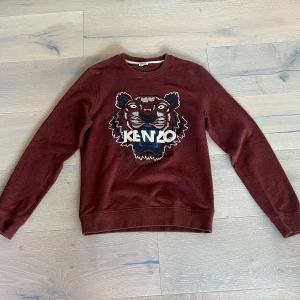 Vinröd Kenzo tröja med tigerbroderi - Hej! Säljer en vinröd Kenzo tröja i storlek M med det ikoniska tigerbroderiet och Kenzo Paris-text på bröstet. Tröjan har rund hals, långa ärmar och är tillverkad i mjuk bomullsmix. Perfekt för dig som vill sticka ut med en snygg och unik design. Köpt i butik i Stockholm för några årsen. Sparsamt andvänd. Tveka inte en sekund på att höra av dig. Ha en bra dag mvh Leo. Ps pris ej hugget i sten.