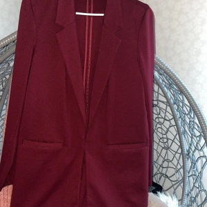 Vinröd kavaj med klassisk krage - Snygg vinröd kavaj med klassisk krage och raka fickor framtill. Stilren och enkel design som passar perfekt till kostymbyxor eller jeans. Kavajen har en mörk, djup färgton och är tillverkad i ett mjukt material som ger en skön känsla.