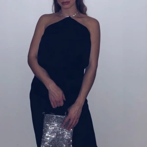 Svart linnetopp med glittrigt band - Svart linnetopp med tunna axelband och ett glittrigt silverfärgat halterneck-band som ger extra bling. Toppen har en snygg draperad front och är croppad i modellen. Perfekt för dig som vill ha en enkel men ändå glam look.