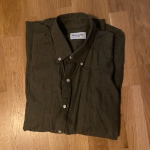 Olivgrön linneskjorta från John Henric - Olivgrön skjorta från John Henric med klassisk krage och vita knappar. Tillverkad i mjukt linne, perfekt för dig som gillar en avslappnad men stilren look. Långärmad modell med normal passform, passar både till jeans och chinos.