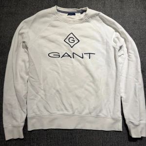 GANT Vit sweatshirt med broderad logga S/M - Vit sweatshirt från GANT med stilren broderad logga i mörkblått på bröstet. Tröjan har rund hals, långa ärmar och mjukt material i bomull. Perfekt för dig som gillar klassisk och enkel stil med en touch av premiumkänsla. Mycket fint skick. Storlek 176 cm / 16 år som motsvarar till S (passar även slim M).