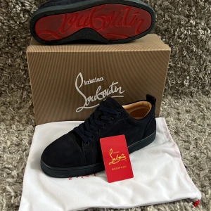 Mörkblå sneakers från Christian Louboutin - Snygga mörkblå sneakers från Christian Louboutin i mocka med klassisk röd sula och broderad logga på hälen. Skorna har rund tå, platt sula och snörning. Insidan är i beige skinn med guldfärgad logotyp. Perfekt för dig som gillar exklusiv streetstyle. 