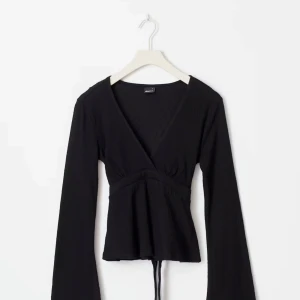 Svart omlottopp med v-ringning - Svart omlottopp från Gina med långa ärmar. Toppen har knyt i midjan och är tillverkad i mjuk bomull med lätt ribbad struktur. Perfekt för dig som gillar stilrena och trendiga plagg med en snygg siluett, pris kan diskuteras💗