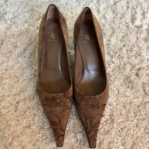Bruna mockapumps med broderi - Snygga bruna pumps i mocka med spetsig tå och låg klack. Perfekta för dig som gillar detaljer och italiensk design. Köpta i Sturegallerian. Använda fåtal gånger och iver skick.🌟