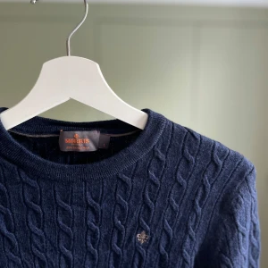 Marinblå kabelstickad tröja Morris - Snygg marinblå kabelstickad tröja från Morris i 100% merinoull. Rund hals och klassisk design som passar perfekt till jeans eller chinos. Tröjan har lång ärm och ett stilrent, tidlöst utseende med strukturstickat mönster.