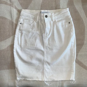 Vit jeanskjol med rå kant från Amisu - Säljer en vit jeanskjol från Amisu med klassisk femficksdesign, knapp och dragkedja framtill. Kjolen är kort och har rå, fransig kant nedtill för en cool vibe. Perfekt för dig som gillar stilrena och trendiga plagg.