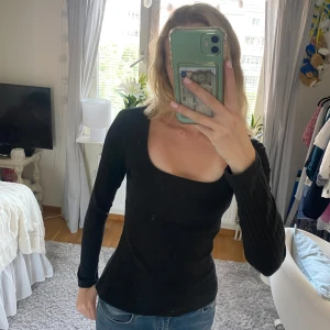 Svart ribbad långärmad topp - Säljer en svart ribbad långärmad topp med fyrkantig ringning. Sitter snyggt och har en slim passform som framhäver figuren. Perfekt att matcha med jeans eller kjol för en clean look. Materialet är mjukt och stretchigt för extra komfort.