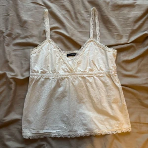 Vit spetsdetaljerad linnetopp Brandy Melville - Supersöt vit linnetopp från Brandy Melville med tunna axelband och spetsdetaljer längs både urringning och nederkant. 