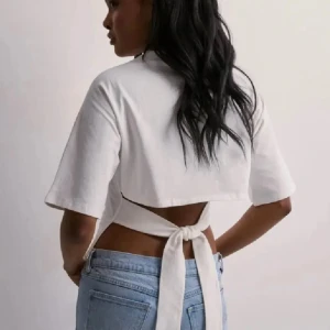 Vit Nelly topp med knyt i ryggen - Säljer en vit Nelly topp med korta ärmar och snygg knytning i ryggen. Toppen har en öppen rygg och är tillverkad i mjukt bomullstyg. Perfekt för dig som gillar trendiga och stilrena plagg med lite edge.