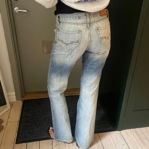 ljusblå bootcut jeans - Säljer ett par ljusblå jeans från Davis med klassisk bootcut passform. Jeansen har snygga detaljer på bakfickorna och är tillverkade i mjukt denimtyg. De har låg midja och raka ben med lätt utsvängning nedtill. Perfekta för en chill och avslappnad stil. Modellen är 171cm. Måtten är midja: 36, längd: 107, innerbenslängd 80cm