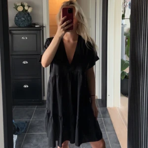 Svart kortklänning med v-ringning - Säljer en svart kortklänning med djup v-ringning och korta ärmar. Klänningen har en loose passform och volangdetaljer nedtill som ger en skön och avslappnad vibe. Perfekt för dig som gillar enkel men snygg stil.