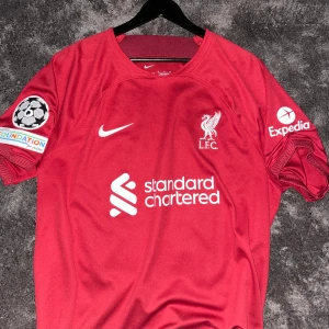 Liverpool FC röd matchtröja  - Liverpool FC matchtröja från Nike i röd Dri-FIT polyester med tryckta loggor, sponsortryck och Champions League-patch på ärmen. Kortärmad modell med Carvalho och nummer 28 på ryggen. Perfekt för dig som vill representera LFC på läktaren eller hemma.