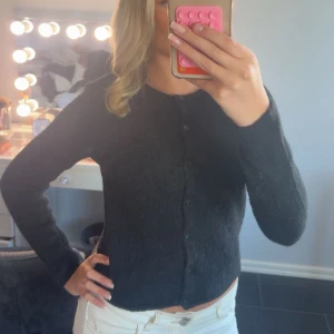 Svart stickad kofta med knappar - Mysig svart kofta med rund hals och knappar hela vägen framtill. Modellen är normal i passningen och har långa ärmar. Materialet är stickat, perfekt att slänga över en topp. Enkel och stilren design som funkar till många outfits. Använt som max 1 gång.