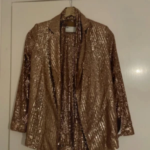 Glittrig guld kavaj och byxor från Zara - Säljer en glittrig guld kavaj från Zara med paljetter över hela jackan och byxorna . Kavajen har klassisk krage och lång ärm, perfekt för att sticka ut på nästa event. Snygg oversized passform och riktigt coolt statement-plagg för dig som gillar att glänsa. Utsvängda byxor till