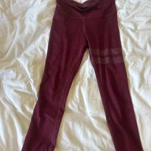 Vinröda leggings från Stronger - Snygga vinröda leggings från Stronger med hög midja och två diskreta ränder på ena benet. Tillverkade i stretchigt material med 85% polyester och 15% spandex, perfekta för träning eller chill. Superskön passform och stilren design.