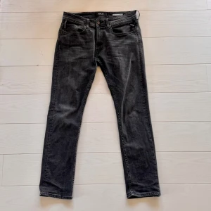 Replay svartgråa jeans - Snygga Replay Dave jeans i svart tvättad denim med klassisk femficksdesign. Speciell modell med Slim/regular passform och raka ben. Jeansen har normal passform och tydliga sömmar på bakfickorna. Perfekta för dig som gillar stilrena och tidlösa jeans med en modern touch. Strl: 31/32