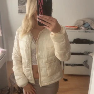 Beige quiltad pufferjacka - Säljer en beige pufferjacka med quiltad design och rund hals. Storleken är 170. En liten skavank ibak på tröjan men knappast syns. Jackan har knappar framtill och två fickor. Perfekt för dig som gillar en clean och chill stil. Materialet är syntet och jackan är långärmad med en loose passform.