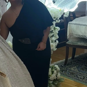 Svart långklänning med oneshoulder - Säljer en elegant svart långklänning med oneshoulder-design och asymmetrisk ärm. Klänningen har en snygg detalj i midjan med glittrande bälte och ett stilrent, figurnära fall. Perfekt för dig som vill sticka ut med en sofistikerad look.