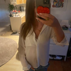 Vit långärmad skjorta med tryck i ryggen - Säljer en vit skjorta med lång ärm och klassisk krage. Skjortan har en bröstficka och ett stort tryck på ryggen som gör den unik. Materialet känns lätt och luftigt, perfekt för dig som gillar stilrena plagg med en twist. Knappar framtill.