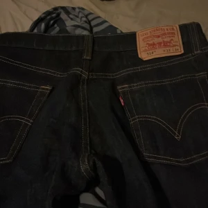 Levi's 514 Slim Straight Jeans - Snygga Levi's 514 jeans i en klassisk mörkblå färg. Dessa jeans har en slim straight passform och är perfekta för en stilren look. De har de ikoniska bakfickorna med kontrastsömmar och en knappgylf.