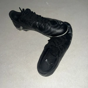 Svarta Puma fotbollsskor med vita detaljer - Snygga svarta fotbollsskor med vita detaljer och snörning. Perfekta för fotbollsplanen med en stilren design och bra grepp.