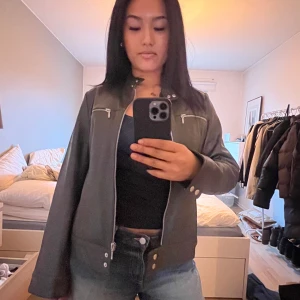 Militärgrön skinnjacka med dragkedjor - Snygg militärgrön skinnjacka med dragkedjor och ståkrage. Jackan har en stilren design med två bröstfickor och en knappdetalj vid kragen. Perfekt för en cool och avslappnad stil.