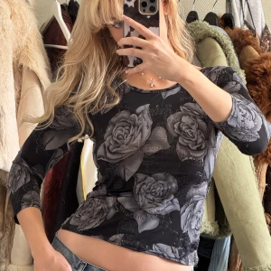 Svart och grå blommig topp - Snygg svart topp med grått blommönster. Toppen har trekvartsärmar och en tight passform, perfekt för en stilren look. Köpt secondhand 