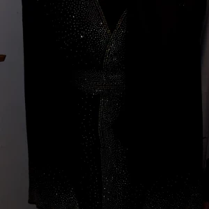 Svart klänning med glittriga detaljer - Elegant svart klänning med glittriga detaljer som ger en lyxig känsla. Klänningen har långa ärmar och ett vackert mönster av små glittrande prickar. Perfekt för speciella tillfällen.