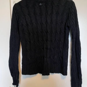 Svart stickad tröja från Vila - Säljer en svart stickad tröja från Vila Tröjan har ett snyggt flätmönster och är tillverkad i en blandning av akryl och ull. Perfekt för kyligare dagar med sin långärmade design.