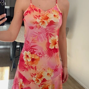 Blommig sommarklänning - Säljer en färgglad sommarklänning med blommigt mönster i rosa, orange och gult. Klänningen är ärmlös med smala axelband och har en kort längd som passar perfekt för varma dagar. Storlek 164cm men passar en större XS eller en S. I väldigt bra skick. 