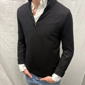 Svart tröja med dragkedja från Riley - Snygg svart tröja från Riley med dragkedja vid halsen. Perfekt för en stilren look. Tröjan har långa ärmar och en klassisk passform. Ett mångsidigt plagg för garderoben. Storlek S. Bra skick, inga defekter. Modellen är 182cm/67kg