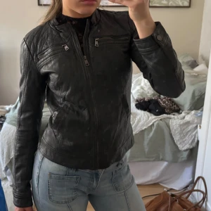 Svart skinnjacka med dragkedja - Snygg svart skinnjacka med dragkedja och två bröstfickor med dragkedjor. Jackan har en tight passform och långa ärmar, perfekt för en cool look. Den har en stilren design som passar till många olika outfits.