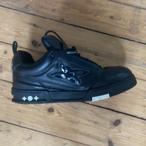 LV SKATE SVARTA - Snygga svarta sneakers från Louis Vuitton med unika detaljer och mönster. Skorna har en stilren design med snörning och är tillverkade i skinn. Priset kan pratas om