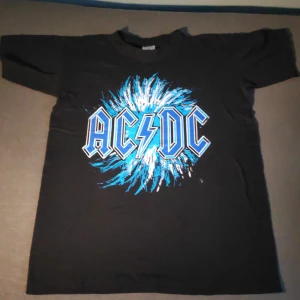 Svart AC/DC t-shirt från B&C Collection - Säljer en svart AC/DC t-shirt från B&C Collection med ett coolt blått och vitt tryck på framsidan. Baksidan har texten 'Highway to Hell'. Perfekt för rockälskare! 🎸