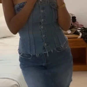 Jeans-korsett från Zara - Säljer en snygg jeans-korsett från Zara med knappar framtill och fransiga kanter. Den har en tight passform och är perfekt för en trendig look. Korsetten är axelbandslös och har en cool vintage-känsla.