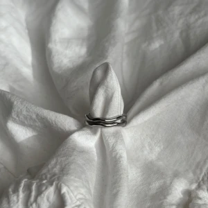 Silverfärgad ring - Elegant silverfärgad ring med en modern, vågig design. Ringen har en öppen design vilket gör den justerbar för olika storlekar.