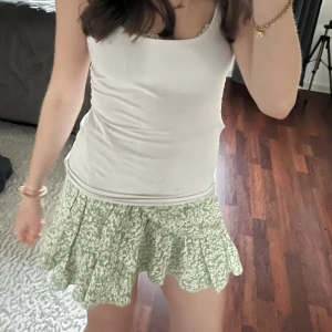 Grön blommig kjol med volang - Säljer en söt grön blommig kjol med volangdetaljer. Kjolen har en omlott-design som ger en fin passform och rörelse. Perfekt för sommarens varma dagar. 🌸